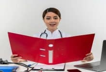 impressed young female doctor wearing medical robe stethoscope sitting desk with medical tools laptop holding looking folder isolated white wall 141793 59643