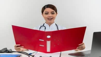 impressed young female doctor wearing medical robe stethoscope sitting desk with medical tools laptop holding looking folder isolated white wall 141793 59643