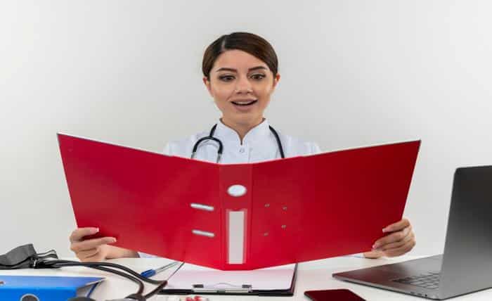 impressed young female doctor wearing medical robe stethoscope sitting desk with medical tools laptop holding looking folder isolated white wall 141793 59643
