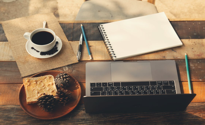 A cozy home office setup with a laptop, coffee, notebook, and toast on a wooden table, representing productive remote work routines